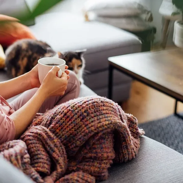 Woman sitting on the couch drinking a coffee with a cat